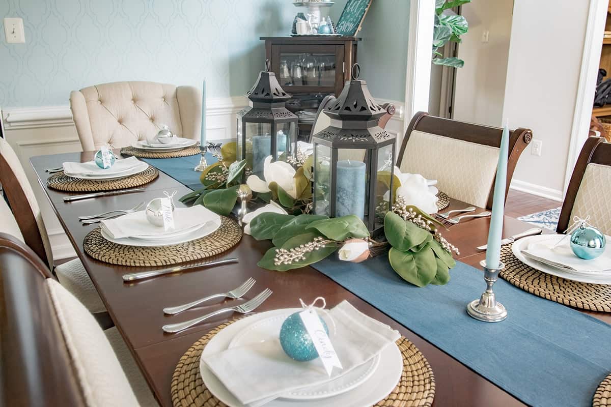 Black lantern centerpiece with magnolia flower garland on blue table runner.
