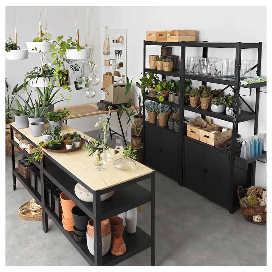 Black IKEA wall shelves and cabinet stands in a gardening room to hold pots and containers.