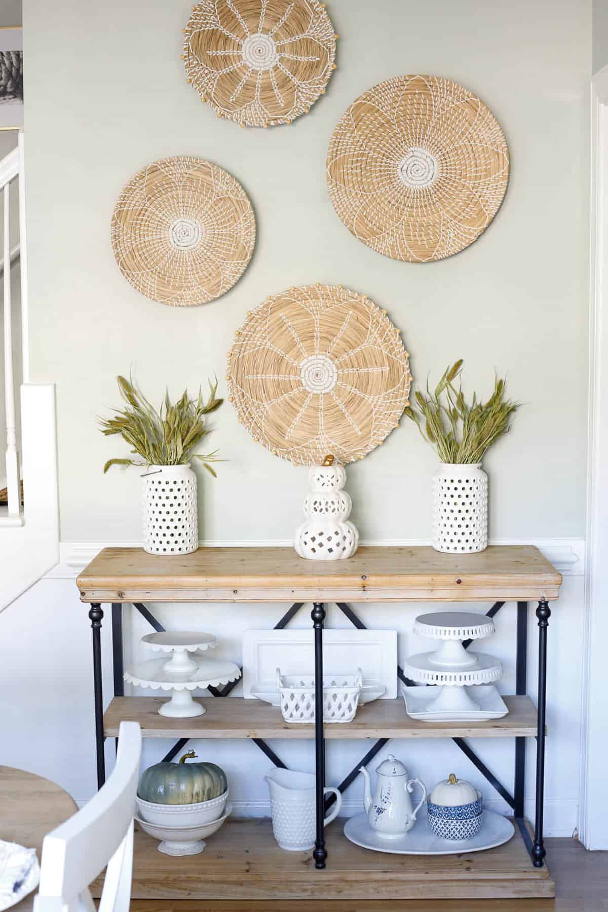 Foyer table with rattan mats hanging above and white glassware on the shelves.