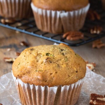 Zucchini Muffin in a paper wrapper with several muffins in the background.