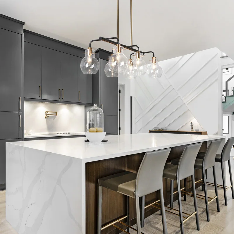 Modern kitchen with waterfall island in white granite and grey cabinets with large light fixture overhanging bar.